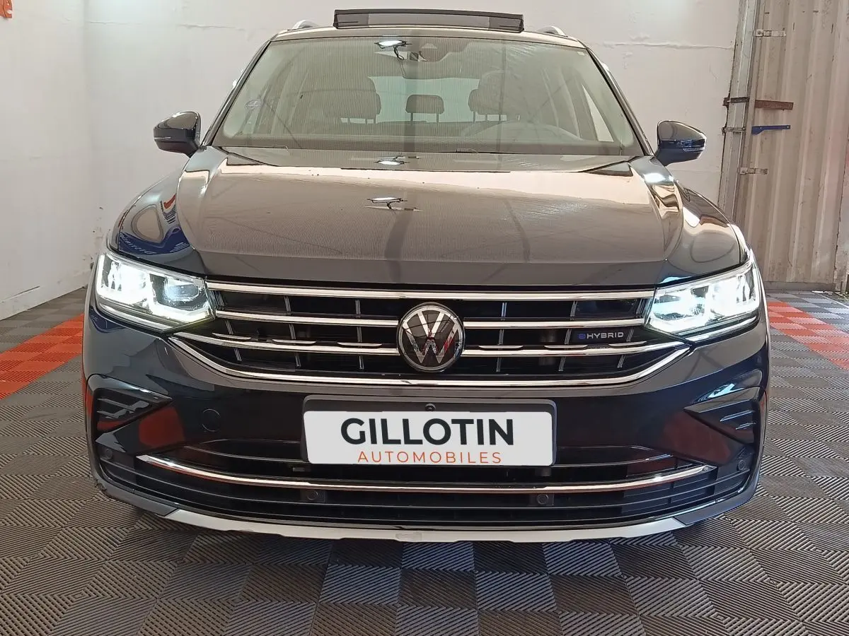 Vue frontale du Volkswagen Tiguan noir hybride rechargeable avec phares LED allumés et calandre chromée.