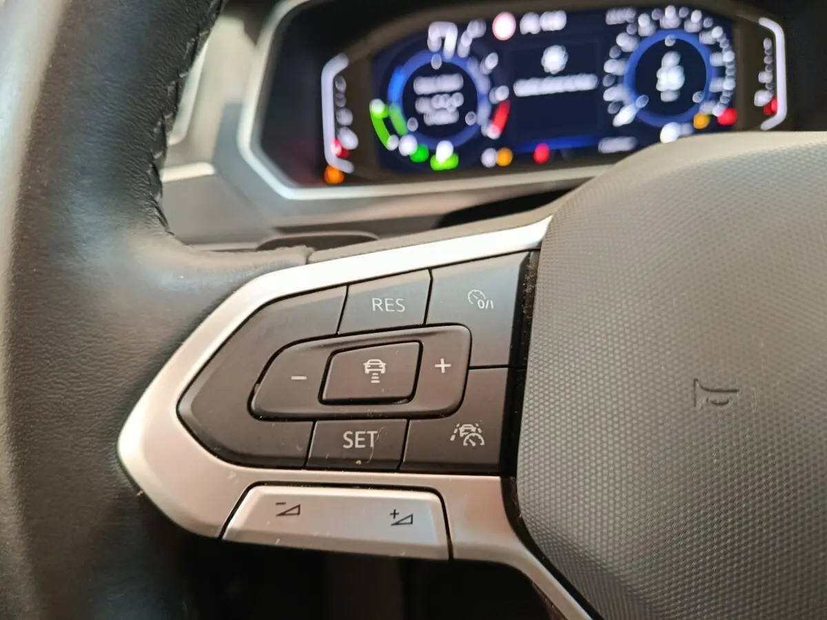 Gros plan sur le volant noir du Volkswagen Tiguan 2022 avec commandes de régulateur adaptatif et tableau de bord numérique flou.