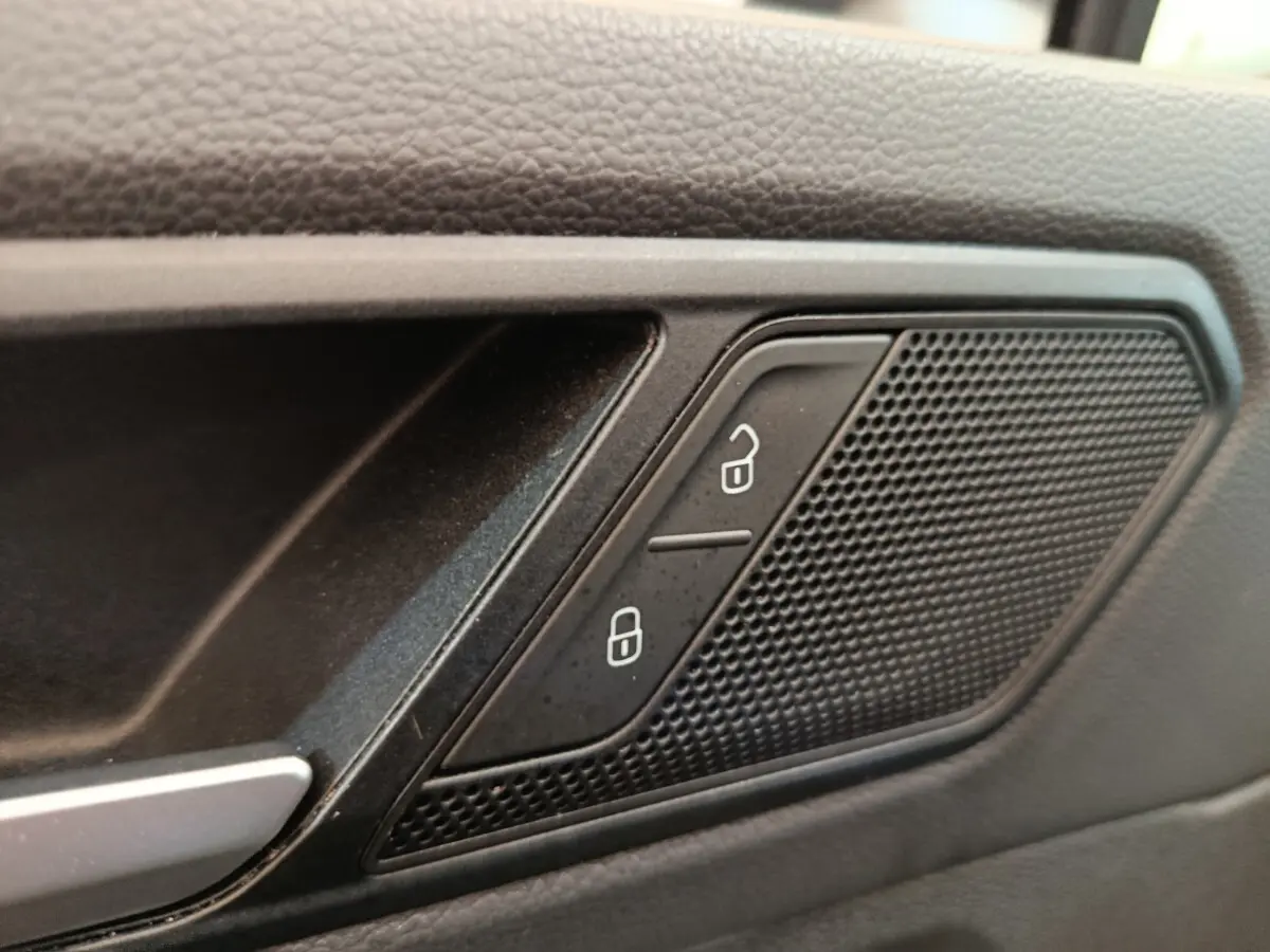 Gros plan sur la commande de verrouillage des portes et haut-parleur intégré dans la porte intérieure noire du Volkswagen Tiguan.
