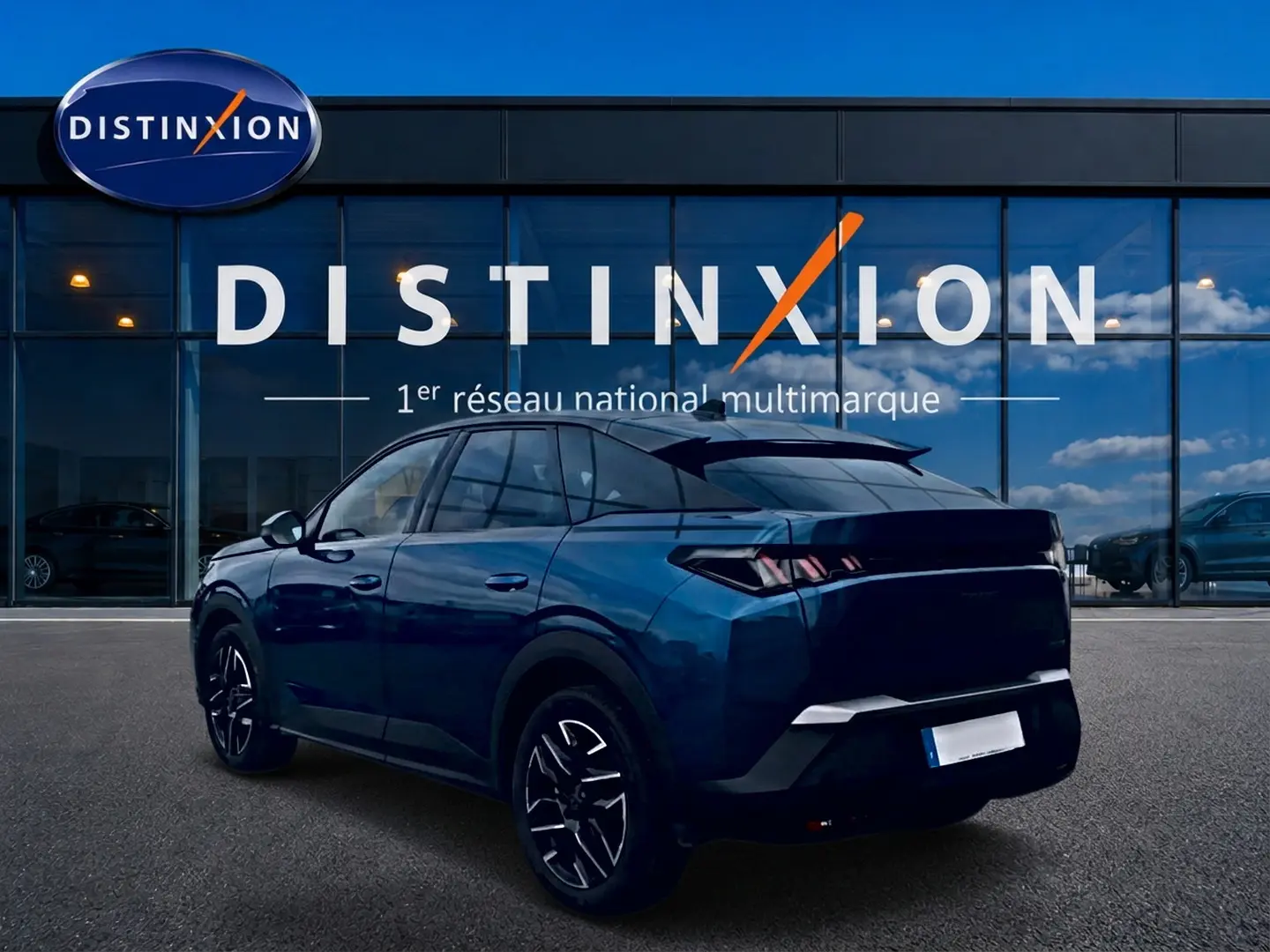 Vue 3/4 arrière d'un Peugeot 3008 bleu 2025 avec jantes alu et becquet arrière, devant une vitrine Distinxion.