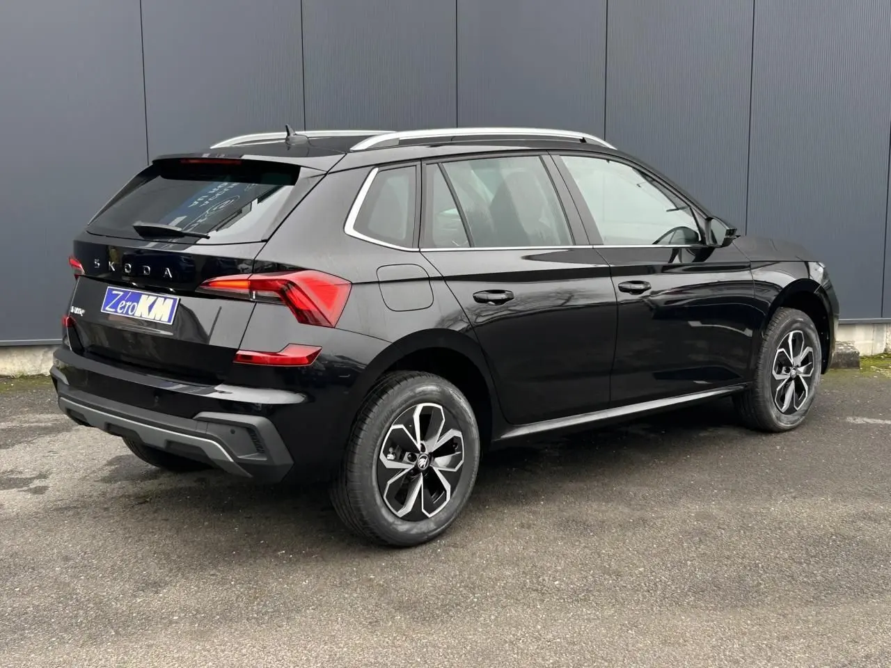 Vue 3/4 arrière droite d'un Skoda Kamiq noir Magic avec jantes alliage et baguettes chromées sur fond urbain.