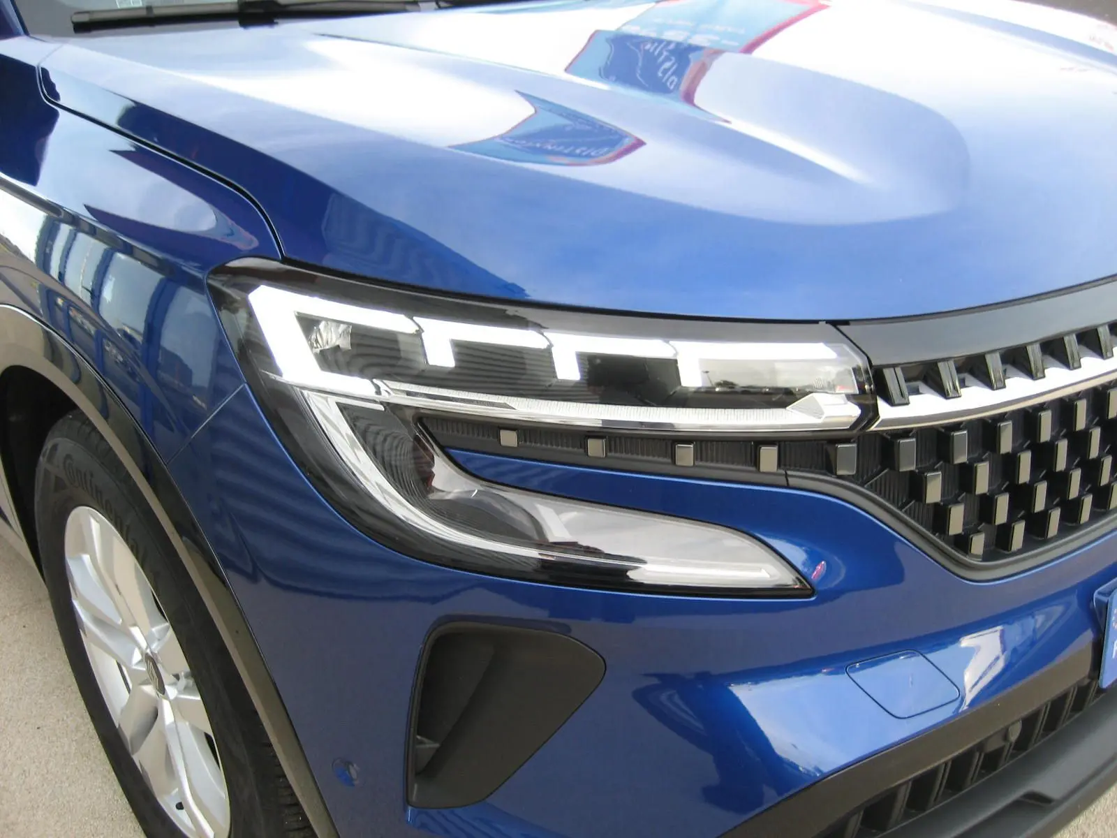 Gros plan sur l'avant droit du Renault Austral bleu Iron, mettant en valeur le phare LED et la calandre noire.