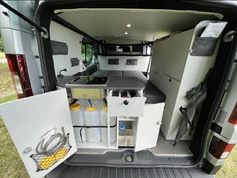 Vue arrière intérieure du Renault Trafic Fourgon gris 2025 aménagé avec kitchenette et rangements ouverts.