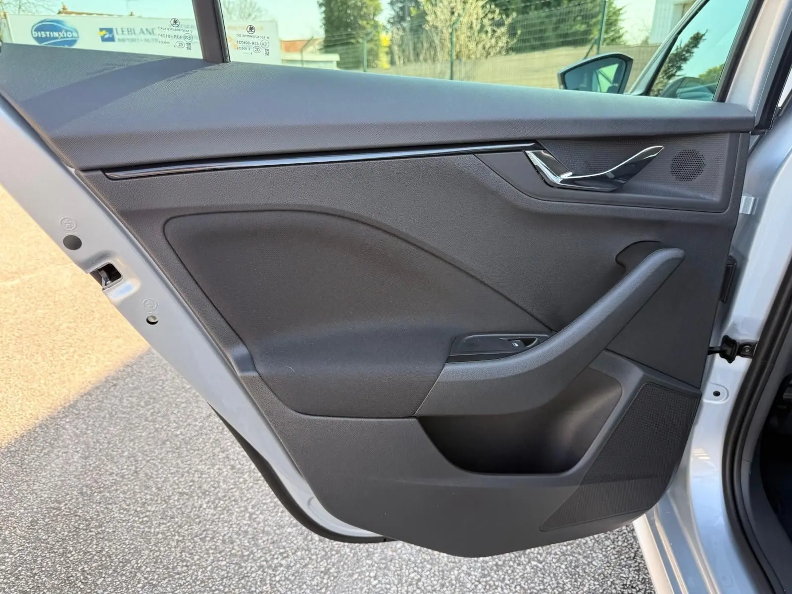 Vue intérieure de la porte arrière gauche d’un Skoda Kamiq gris argent, avec garniture noire et poignée chromée.