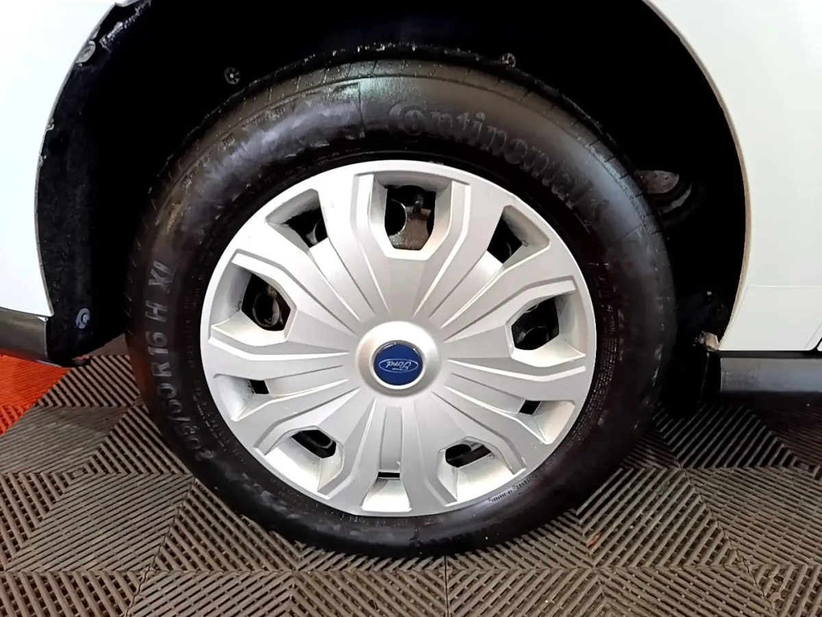 Gros plan sur la roue avant droite blanche du Ford Transit Fourgon avec enjoliveur argenté et logo Ford central.