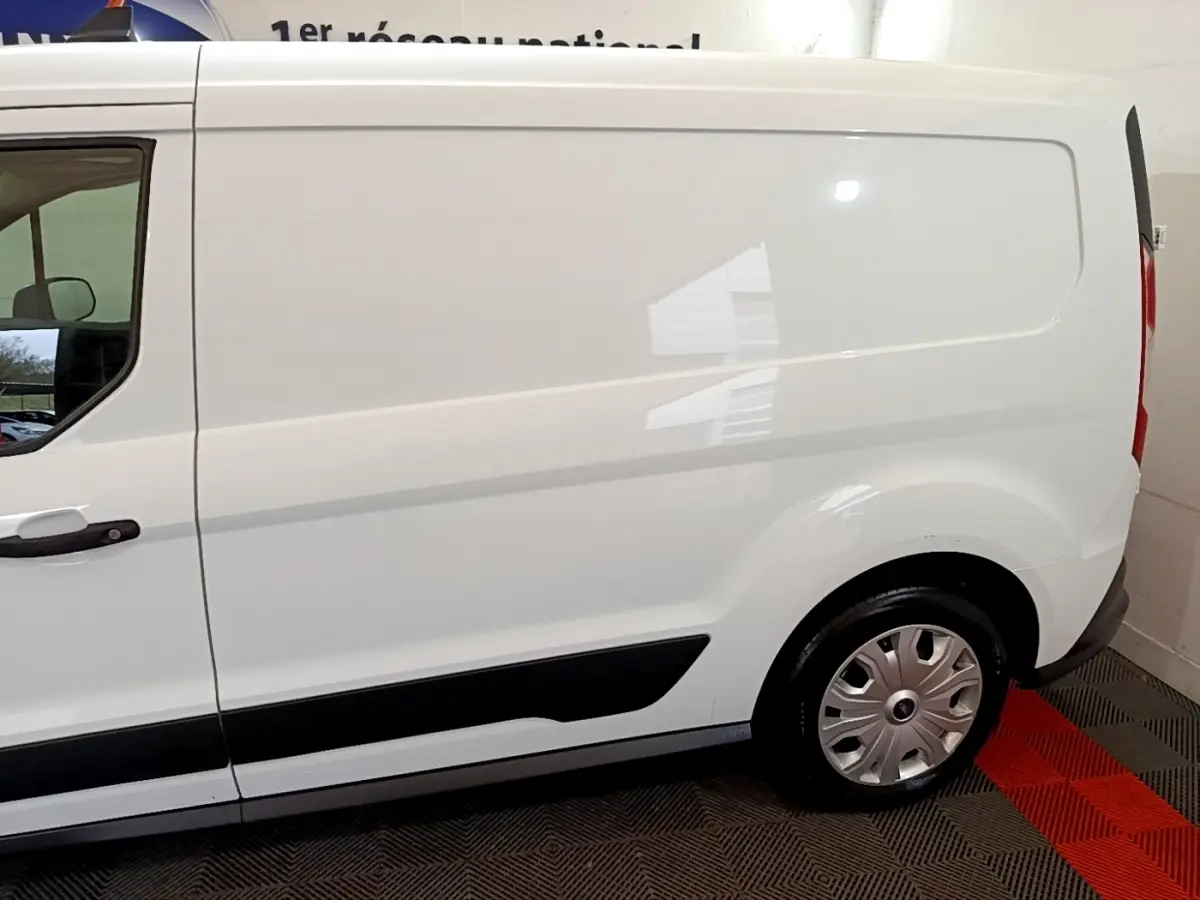 Vue latérale côté gauche d'un fourgon Ford Transit blanc, mettant en valeur la porte coulissante et la roue arrière.