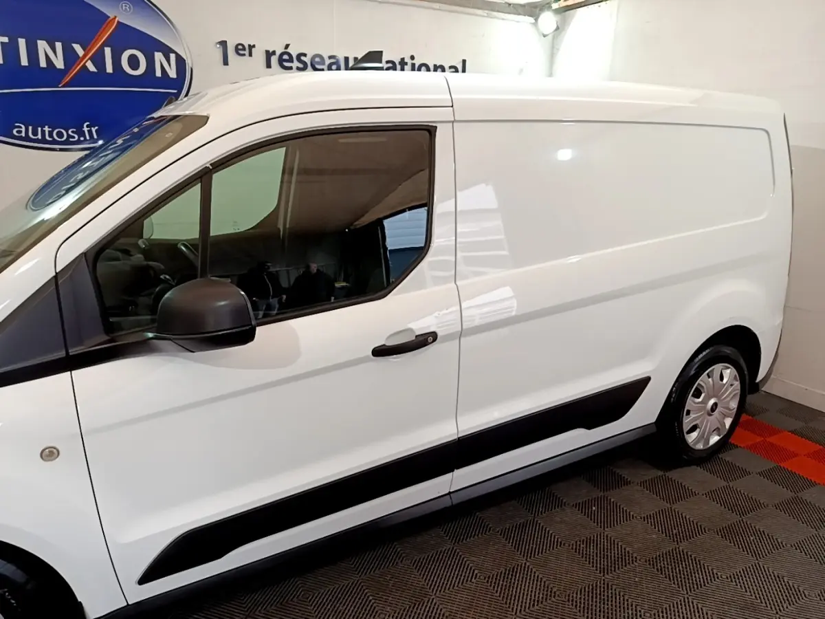 Vue latérale droite d'un fourgon Ford Transit blanc avec rétroviseur noir et protections latérales noires.
