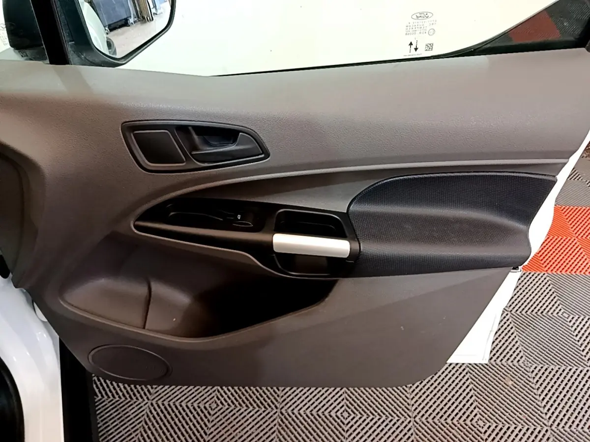 Vue intérieure côté gauche de la porte avant d’un Ford Transit Fourgon blanc, avec poignée argentée et panneau noir texturé.