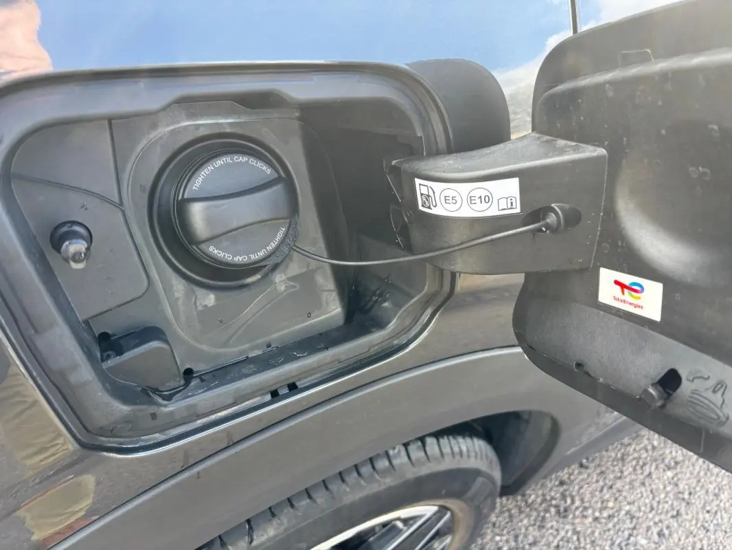 Gros plan sur la trappe à carburant côté gauche d’un Peugeot 3008 gris avec bouchon essence et jante alliage visible.