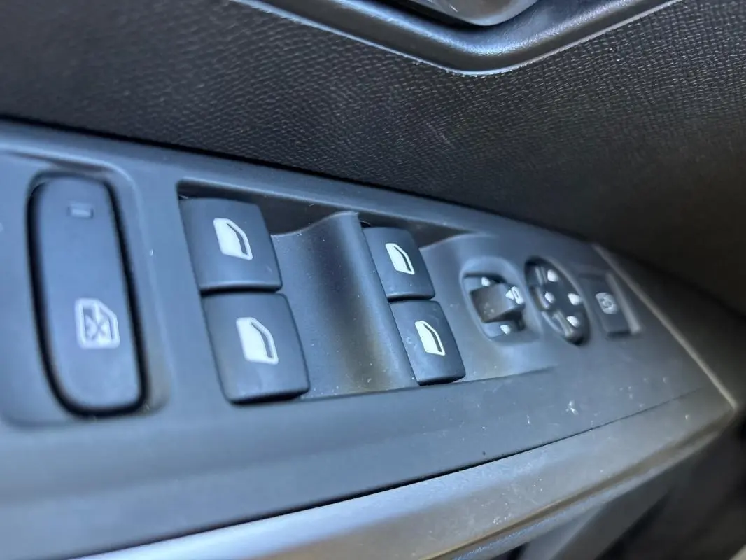 Gros plan sur les commandes des vitres électriques et rétroviseurs côté gauche d’un Peugeot 3008 gris 2025.