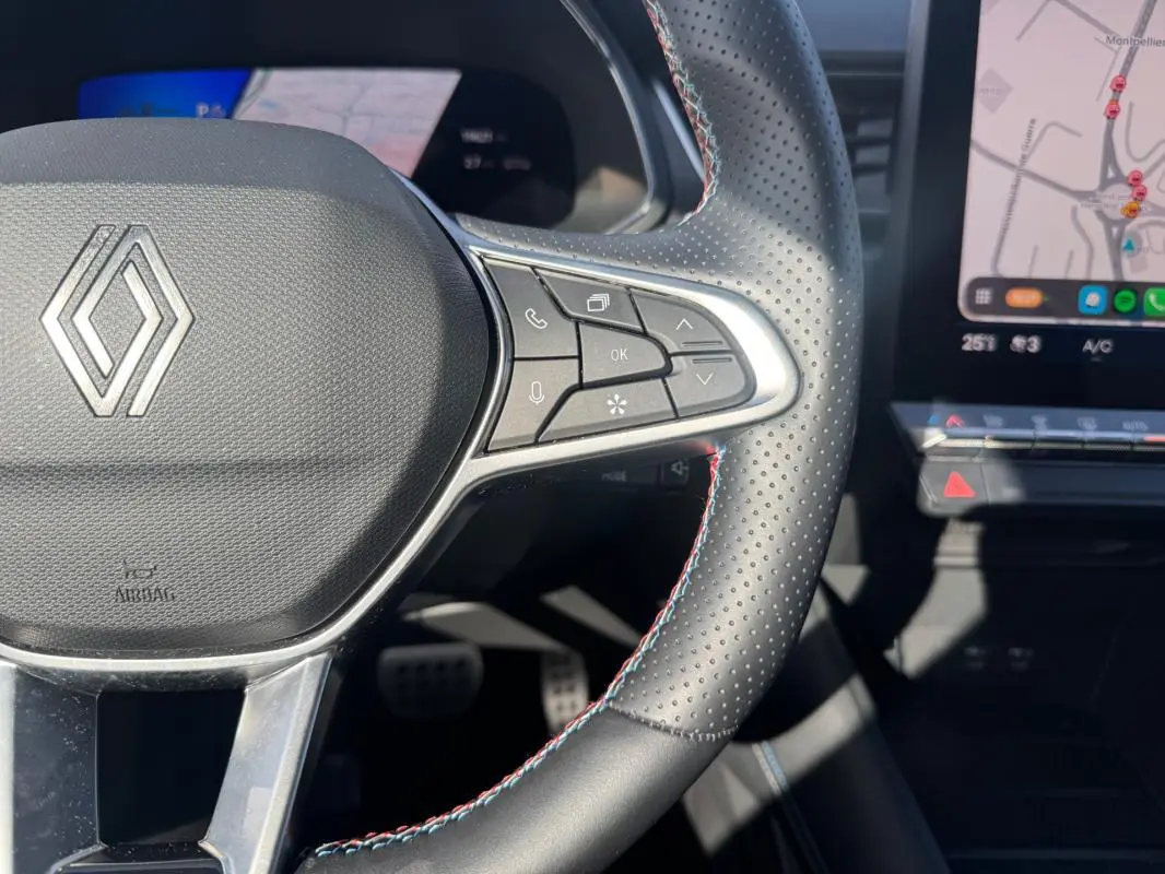 Gros plan sur le volant noir perforé du Renault Symbioz gris clair avec commandes intégrées et écran tactile visible.