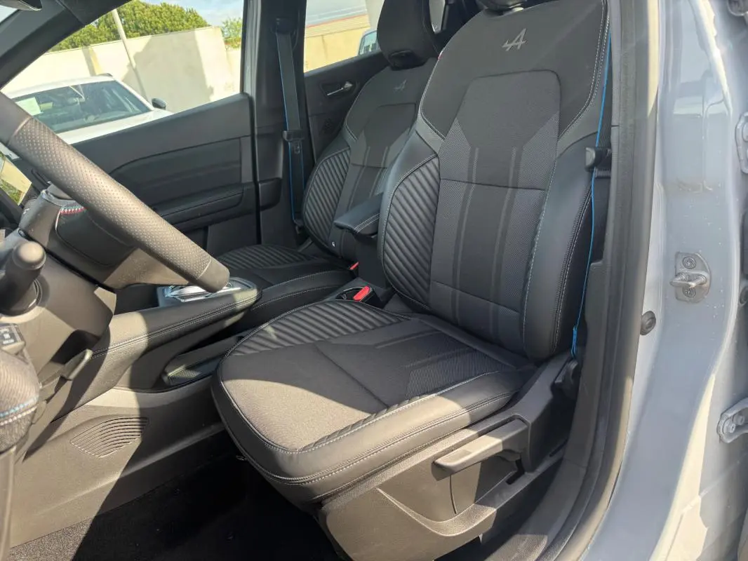 Vue intérieure côté conducteur du Renault Symbioz gris clair, mettant en valeur les sièges noirs avec logo Alpine brodé.