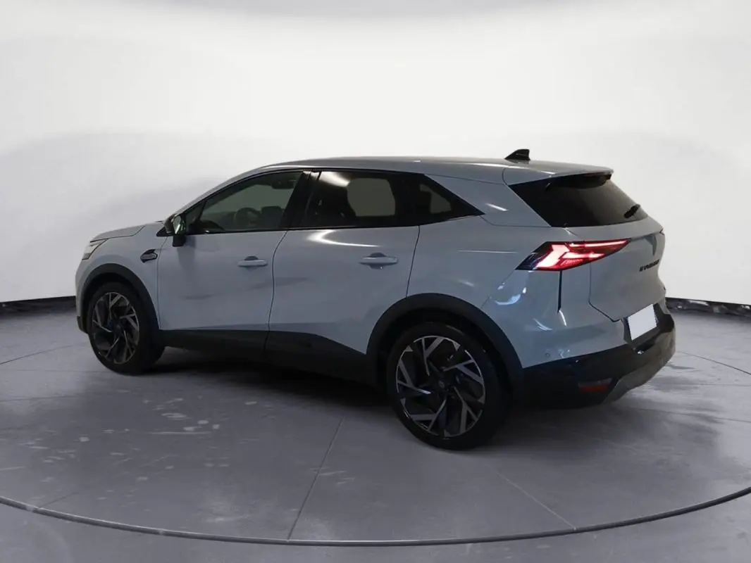 Renault Symbioz gris clair en vue 3/4 arrière droit, avec jantes alliage 19 pouces et feux arrière allumés.