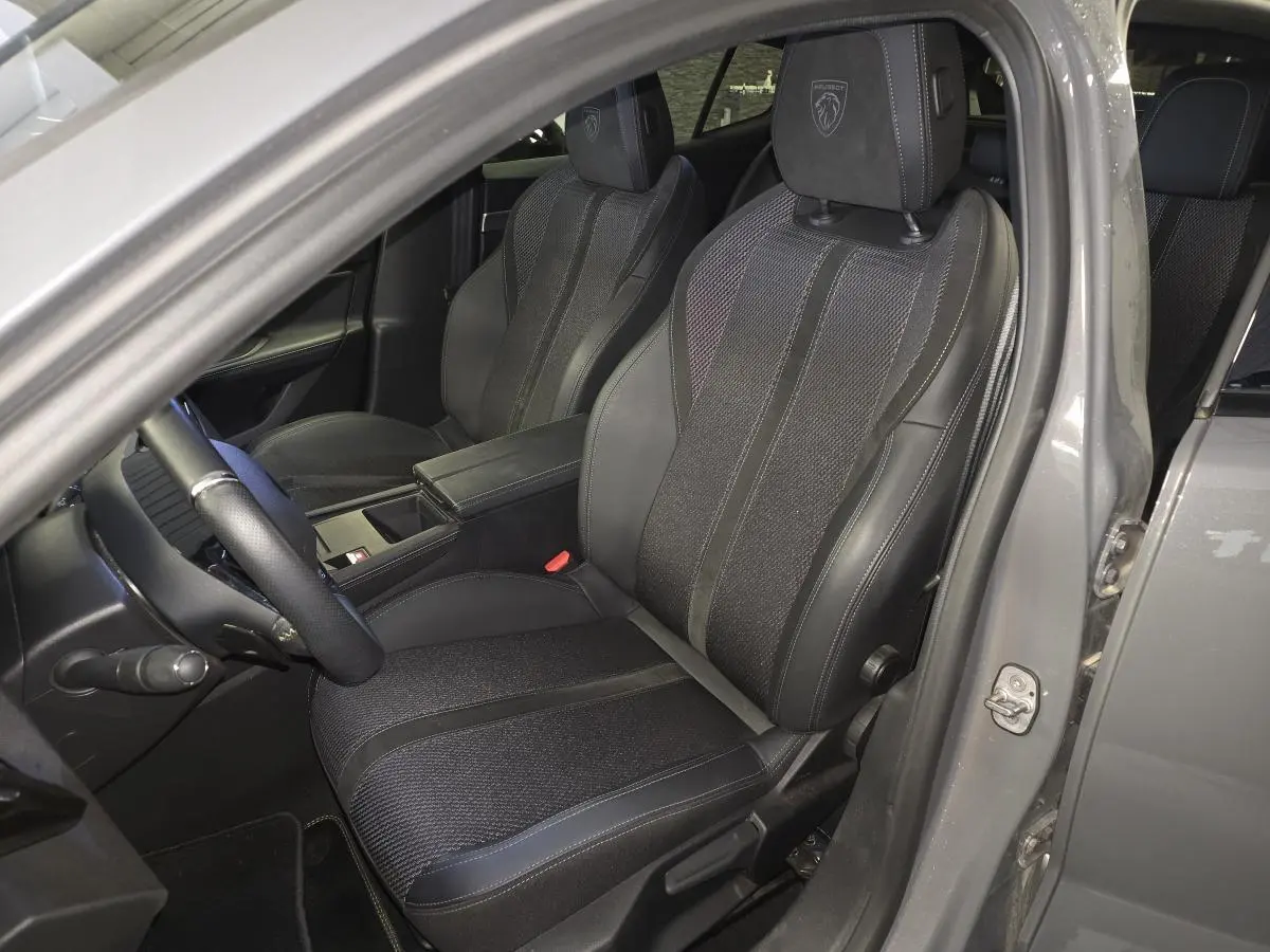 Vue intérieure côté conducteur de la Peugeot 408 gris Selenium, sièges tri-matières avec logo Peugeot brodé sur les appuis-tête.