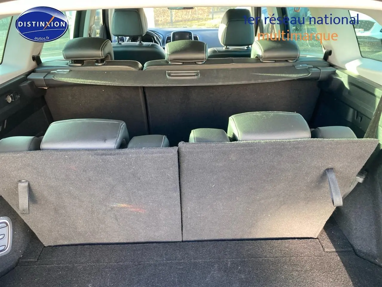 Vue arrière du coffre du Renault Grand Scenic IV bleu, sièges arrière partiellement rabattus et cache-bagages en place.