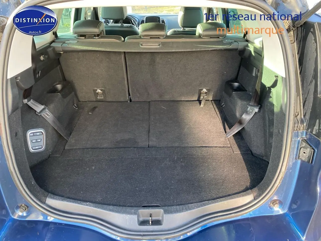 Coffre ouvert d’un Renault Grand Scénic IV bleu, montrant les sièges arrière rabattus et la moquette noire.