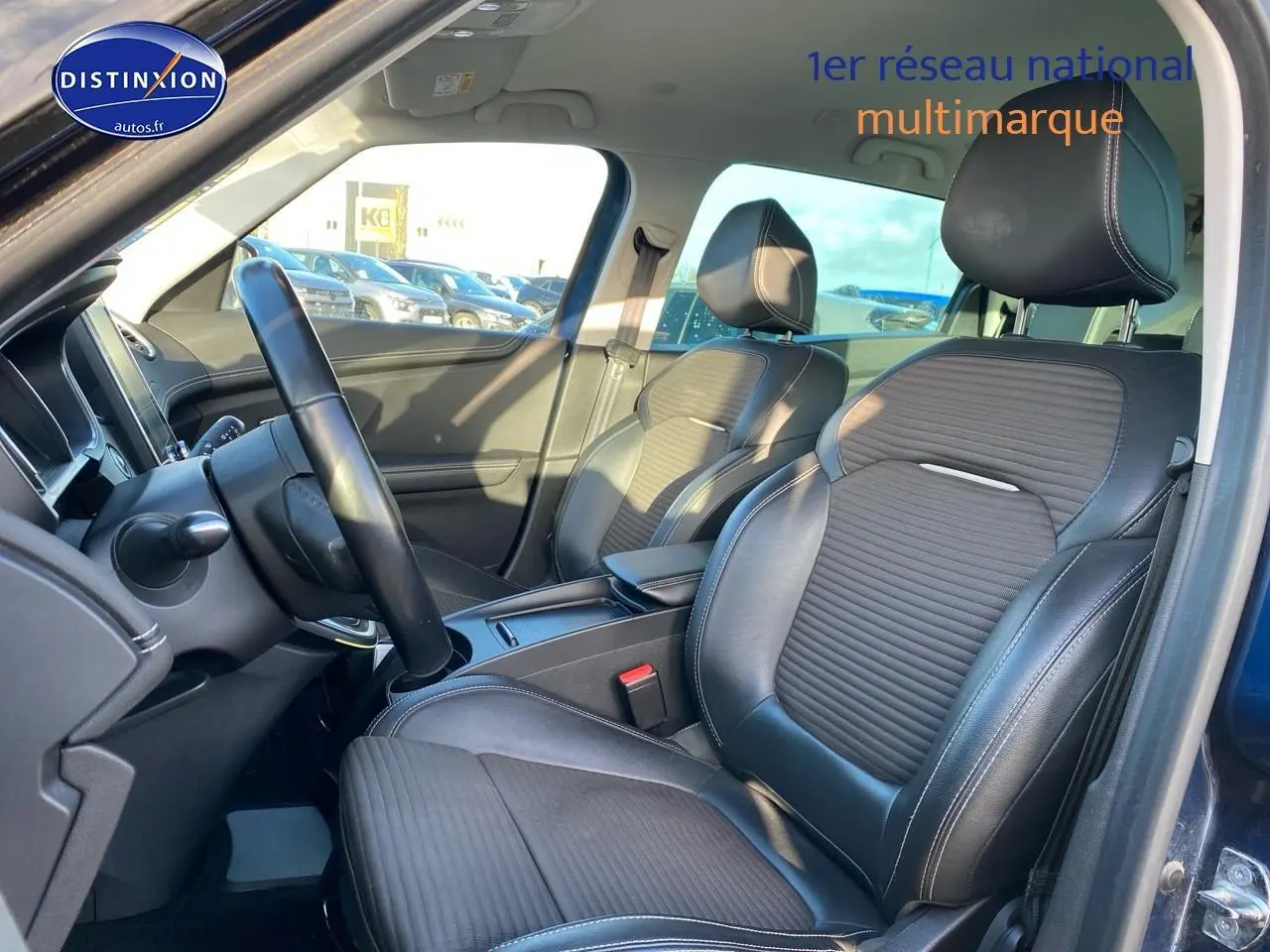 Vue intérieure côté conducteur du Renault Grand Scenic IV bleu, sièges avant en similicuir noir avec surpiqûres blanches.