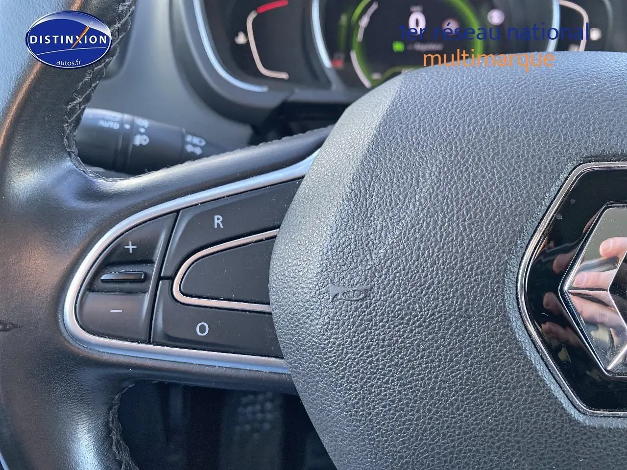 Gros plan sur le volant cuir de la Renault Grand Scenic IV bleu, avec commandes intégrées à gauche et logo Renault visible.