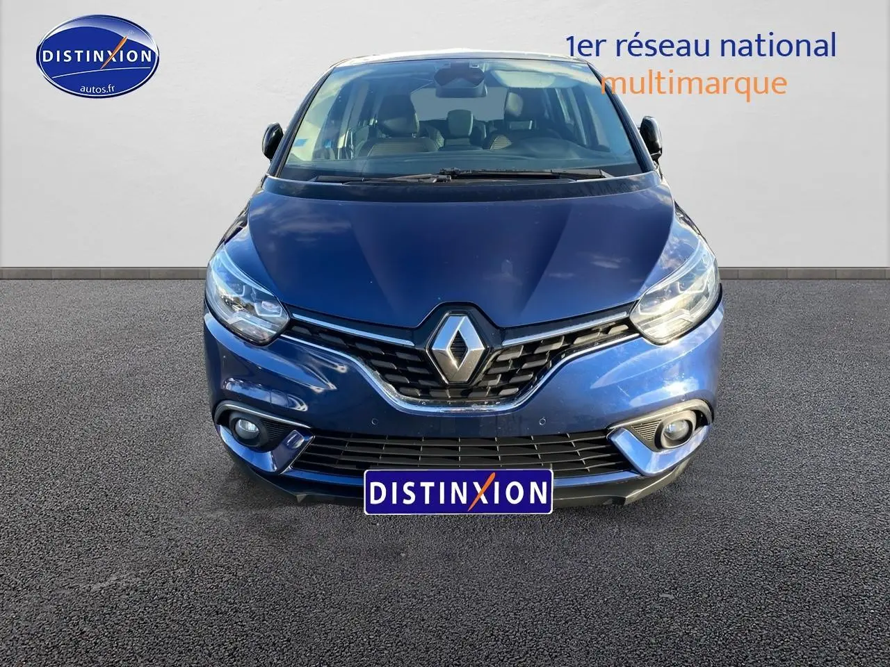 Vue avant d’un Renault Grand Scénic IV bleu avec calandre chromée et feux LED allumés sur fond neutre.