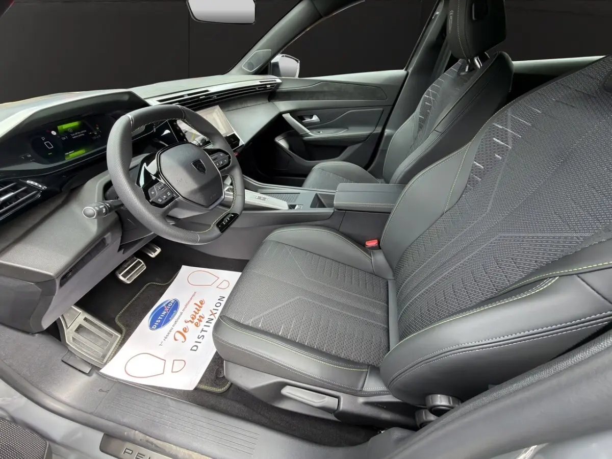 Intérieur avant droit de la Peugeot 308 gris clair, sièges tissu et cuir avec surpiqûres vertes, tableau de bord moderne.