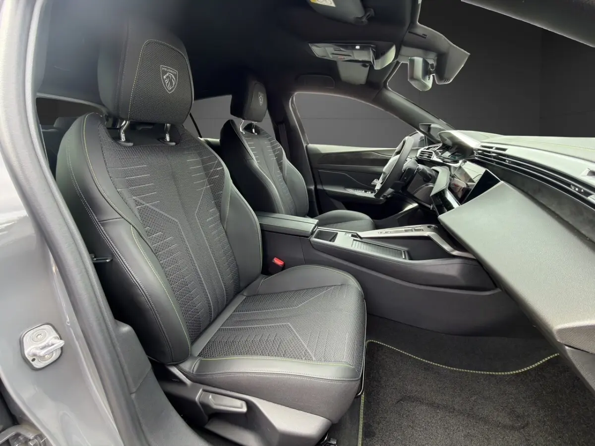 Vue intérieure côté conducteur de la Peugeot 308 gris clair 2026, sièges sport avec logo lion brodé et tableau de bord moderne.