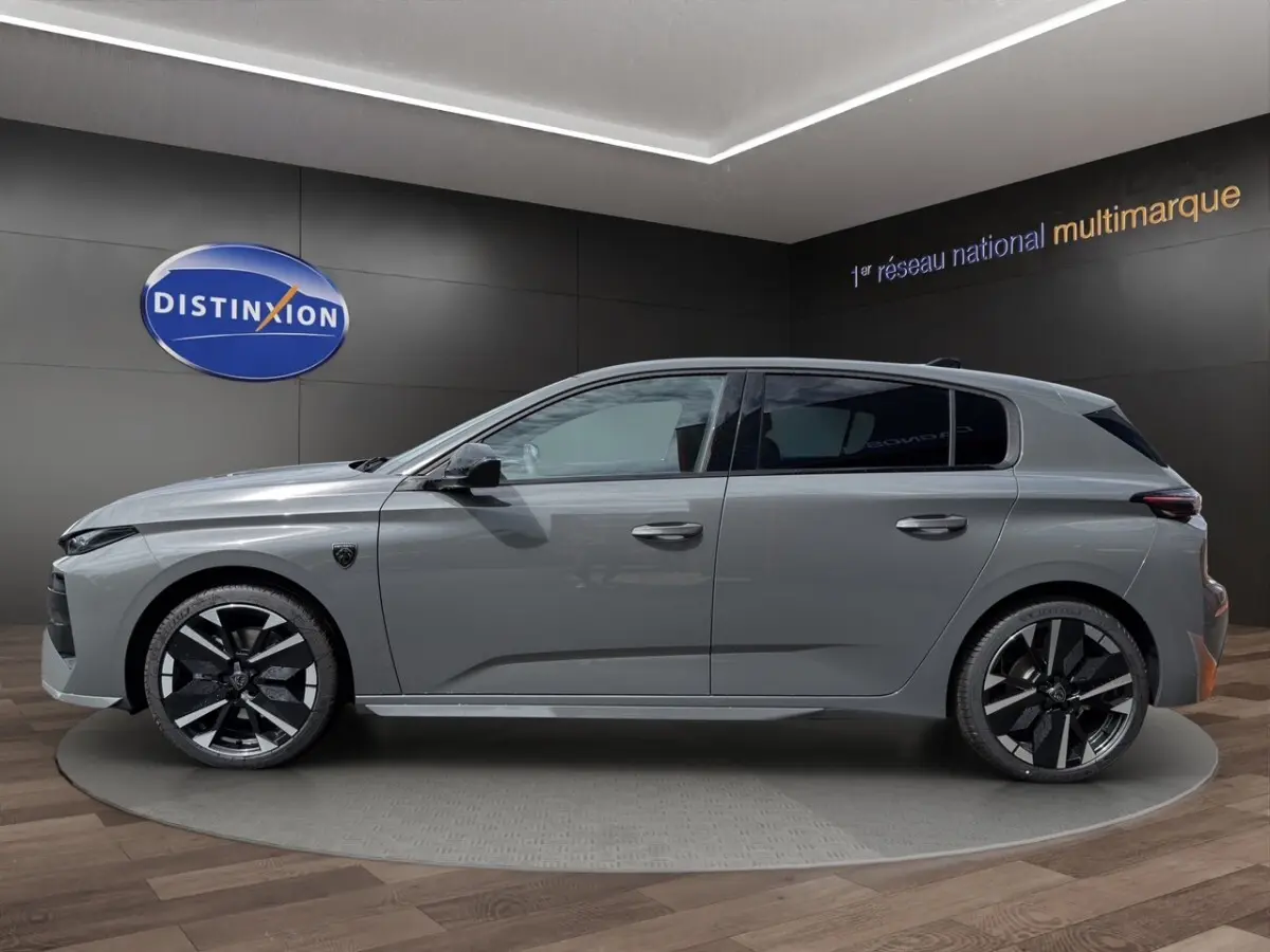 Vue de profil côté gauche d'une Peugeot 308 gris clair 2026 exposée en showroom avec jantes noires et grises distinctives.