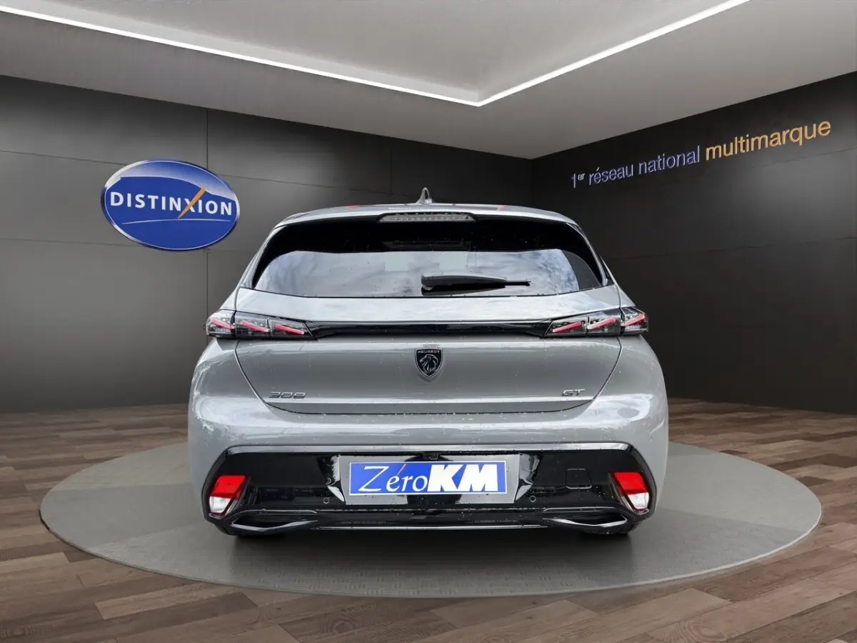 Vue arrière d'une Peugeot 308 GT gris clair avec feux arrière LED et logo noir brillant sur fond showroom.