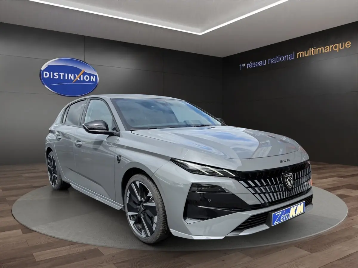 Peugeot 308 gris clair vue 3/4 avant droit, avec calandre noire distinctive et jantes noires brillantes.
