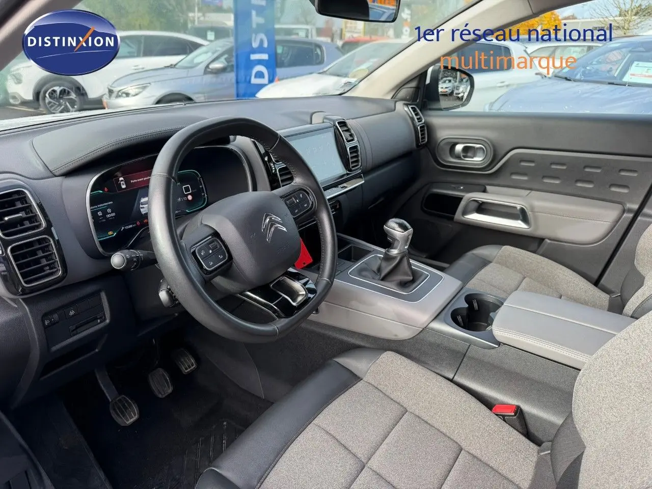Vue intérieure côté conducteur du Citroën C5 Aircross 2019, volant cuir noir et sièges tissu gris avec console centrale grise.