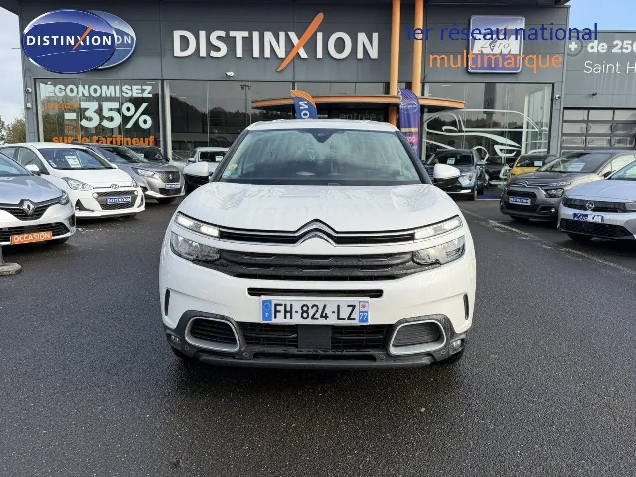 Vue de face d'un Citroën C5 Aircross blanc nacré, avec calandre distinctive et phares LED allumés, sur parking de concession.