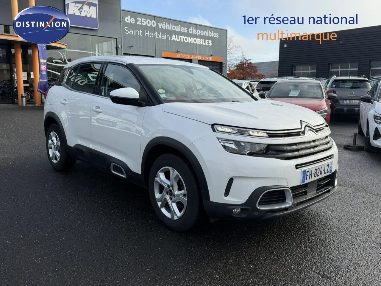 SUV Citroën C5 Aircross blanc nacré vu en 3/4 avant droit sur parking devant concession automobile.