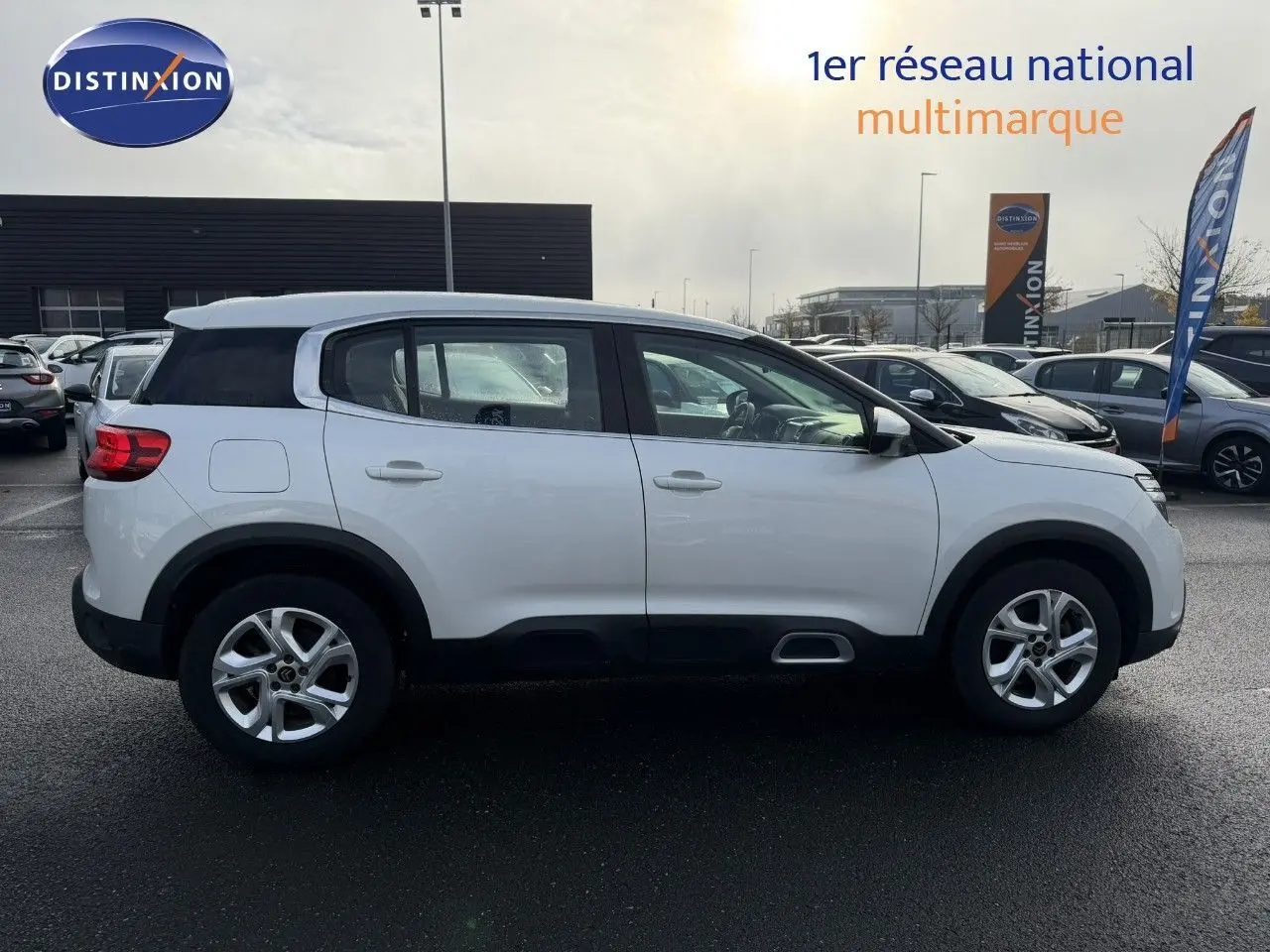Profil latéral droit d'un Citroën C5 Aircross blanc nacré avec jantes alliage et protections noires sur un parking extérieur.