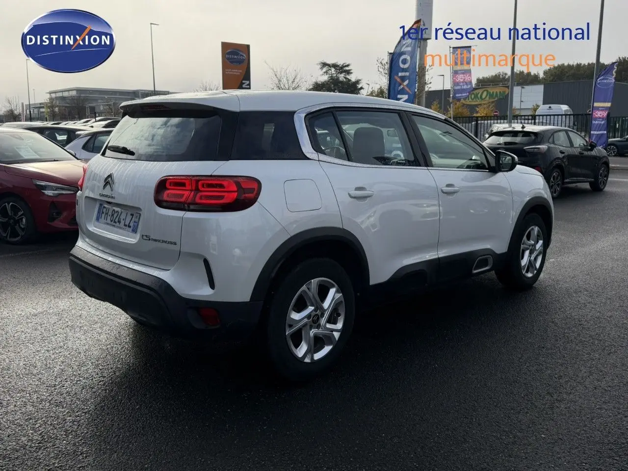 Vue 3/4 arrière droite d'un Citroën C5 Aircross blanc nacré avec feux arrière allumés sur parking extérieur.