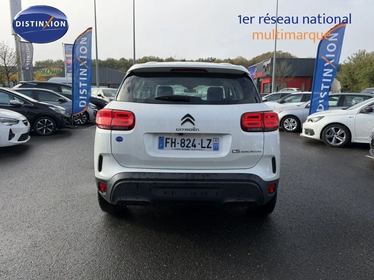 Vue arrière d'un Citroën C5 Aircross blanc nacré garé sur un parking, avec feux arrière allumés et plaques visibles.