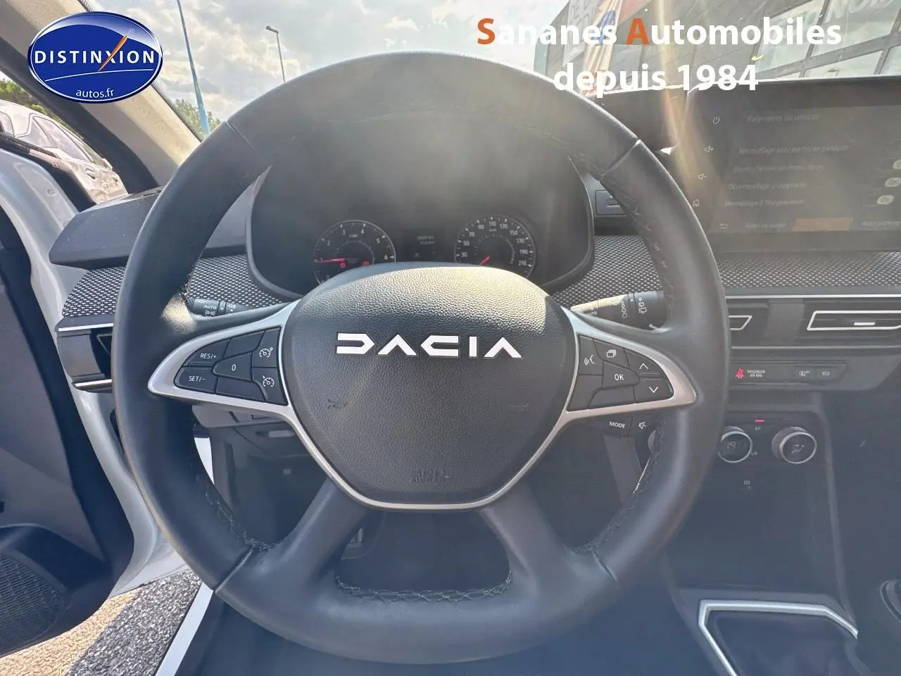 Vue intérieure centrée sur le volant noir DACIA du Jogger blanc, avec tableau de bord et écran tactile visibles à droite.