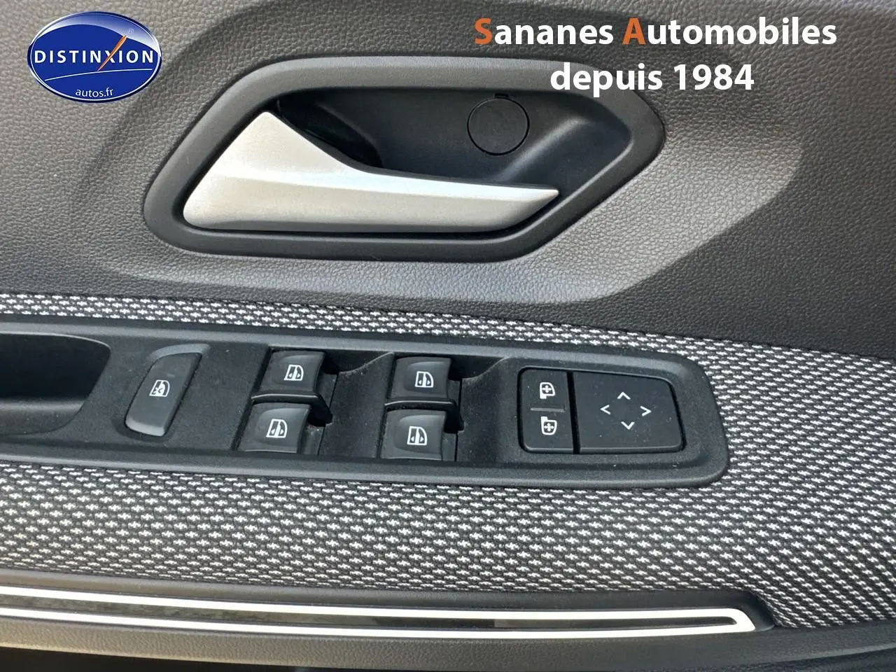Gros plan sur la commande des vitres électriques et la poignée intérieure côté conducteur du Dacia Jogger blanc.