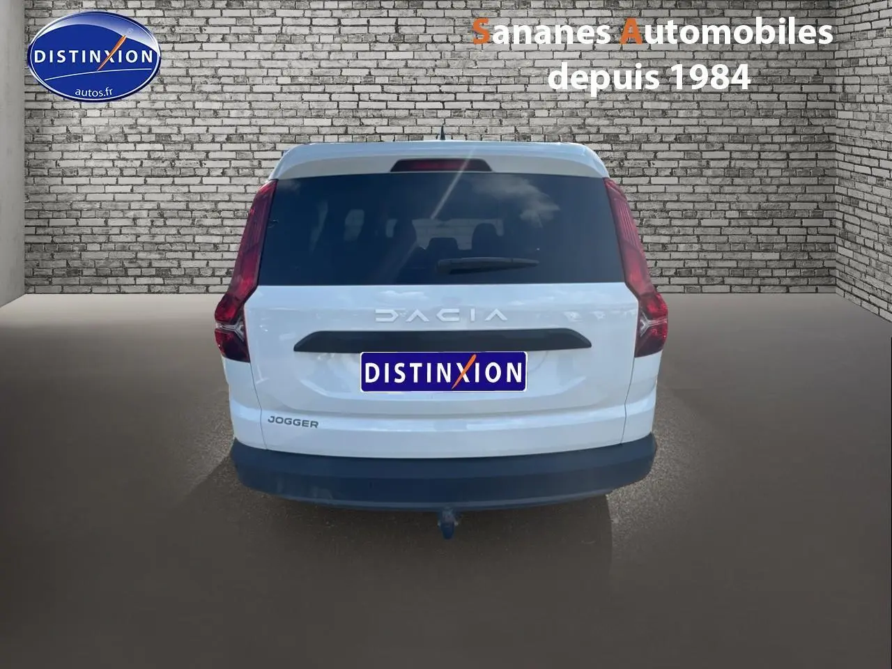 Vue arrière d'un Dacia Jogger blanc avec attelage et vitres arrière surteintées sur fond de mur en briques.