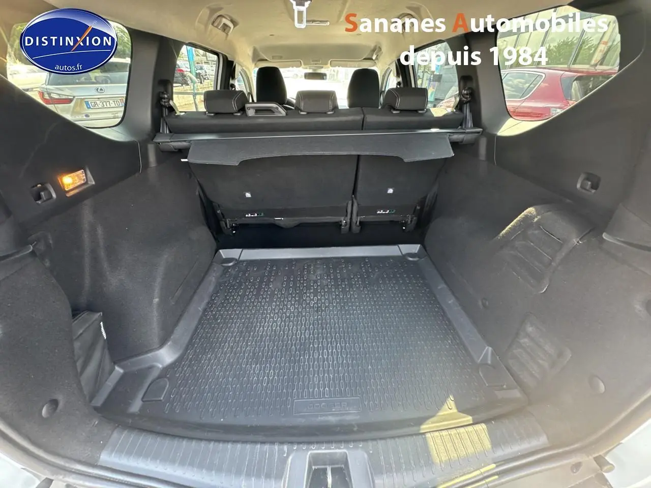 Coffre ouvert du Dacia Jogger blanc, vue intérieure arrière montrant la banquette rabattable et le tapis de coffre noir.