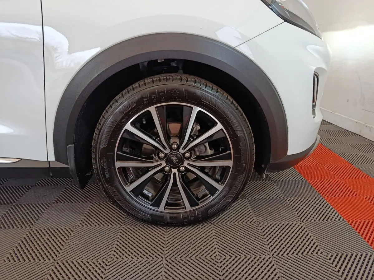 Gros plan sur la roue avant droite noire et argentée du Ford Puma blanc, avec passage de roue en plastique noir.