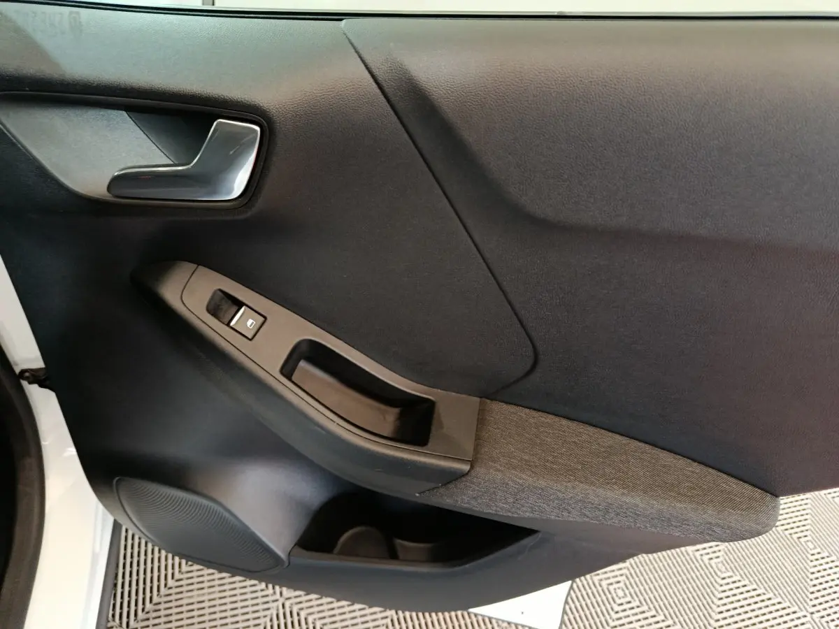 Vue rapprochée de la porte avant gauche noire avec poignée argentée et commande de lève-vitre sur Ford Puma blanc.