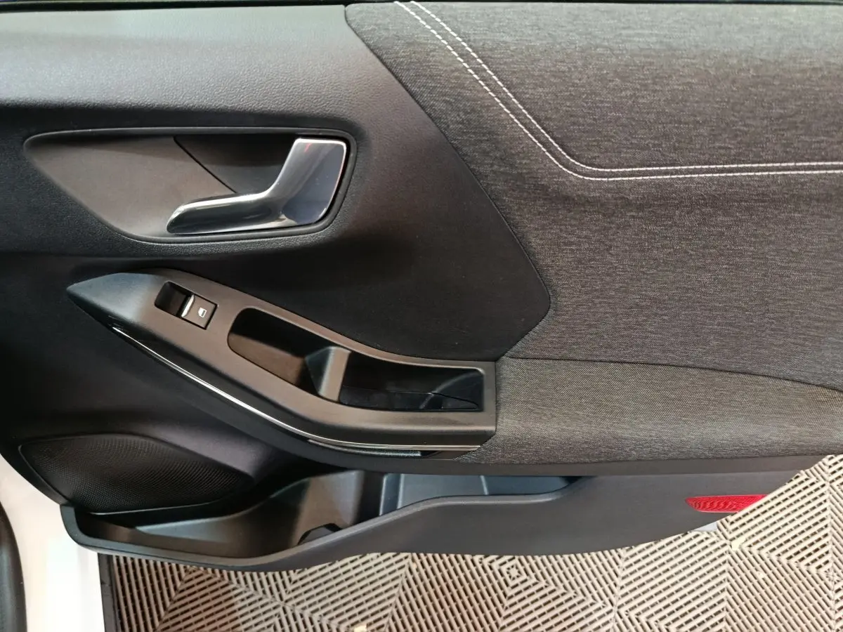 Gros plan sur la porte intérieure côté conducteur du Ford Puma blanc, montrant la poignée et les commandes de fenêtre.