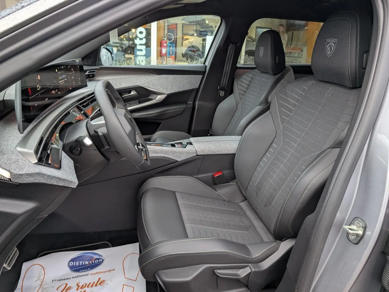 Vue intérieure côté conducteur du Peugeot 5008 gris 2025, sièges tissu et cuir avec logo Peugeot brodé sur appuie-tête.
