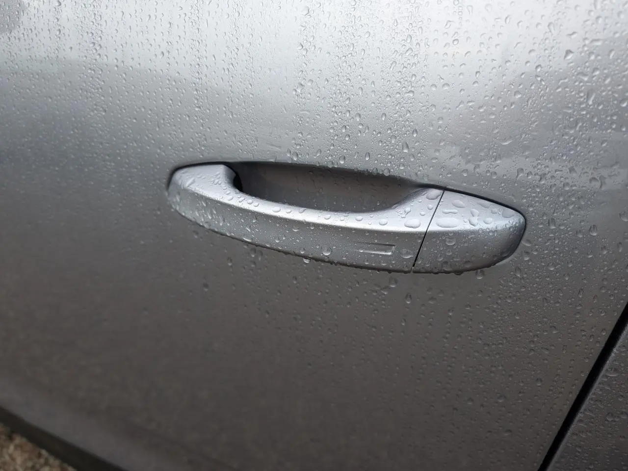 Poignée de porte gris métallisé du Peugeot 5008 2025, couverte de gouttes de pluie, vue en gros plan.