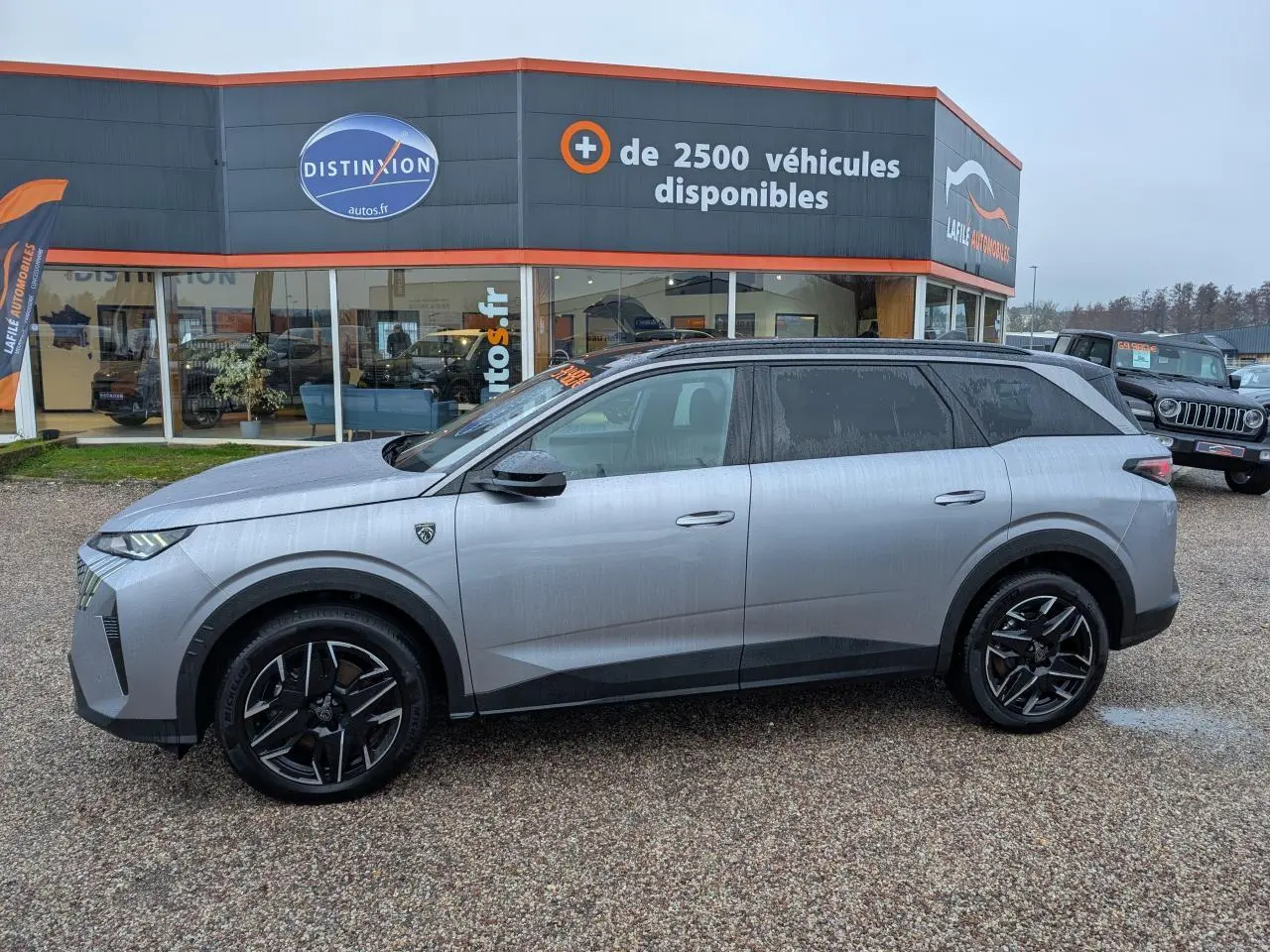 Vue de profil côté gauche d’un Peugeot 5008 gris métallisé 2025 avec jantes alliage noires et toit noir.