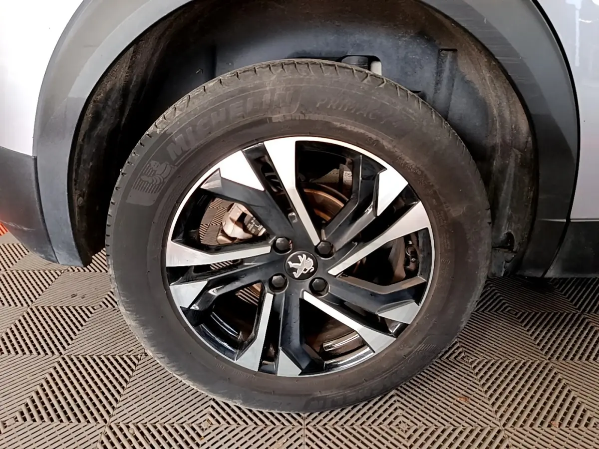 Gros plan sur la roue avant droite d’un Peugeot 2008 gris clair, avec jante alliage noire et argentée.
