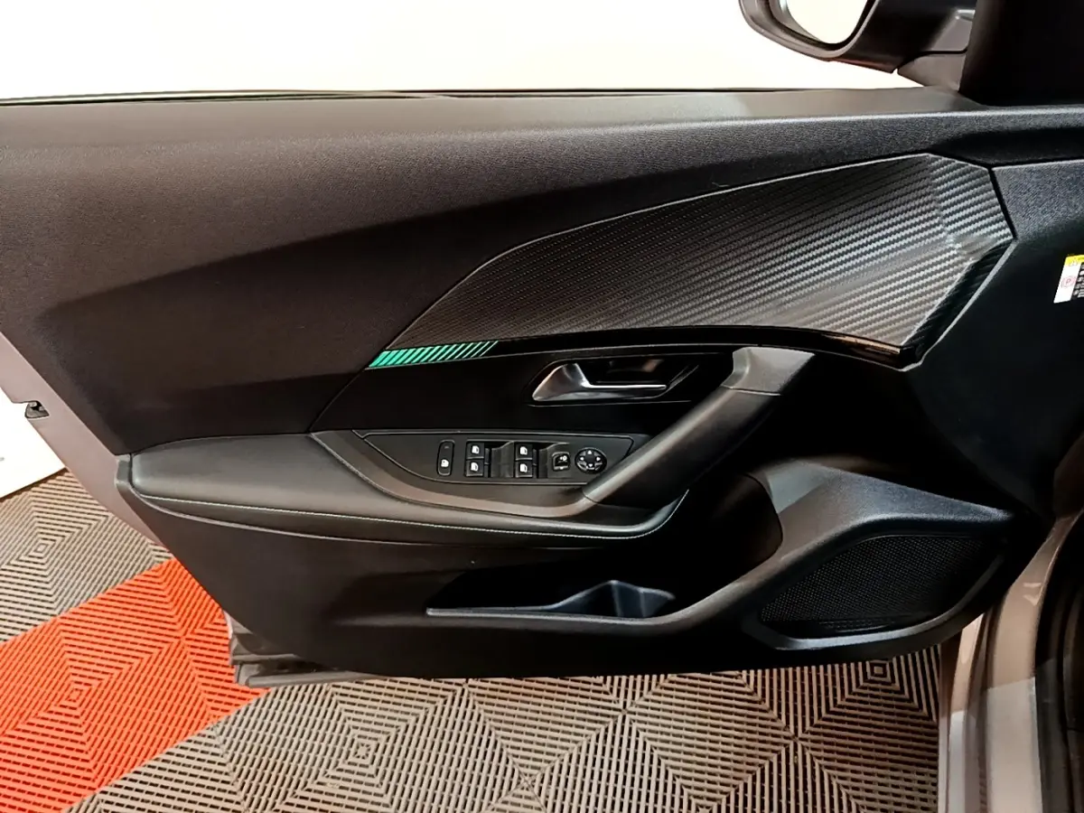 Vue intérieure côté gauche de la porte avant d’un Peugeot 2008 gris clair, avec commandes électriques et décor carbone.