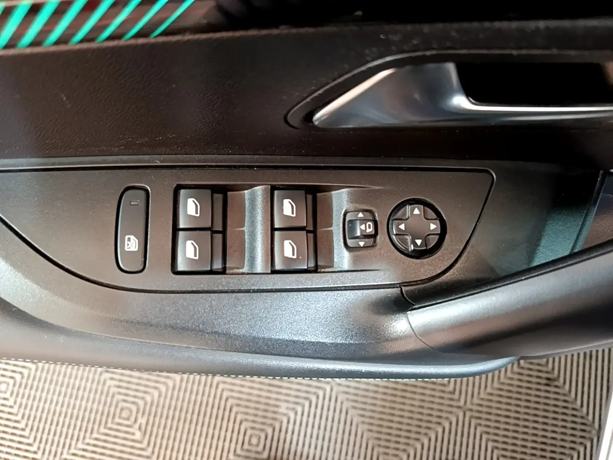 Gros plan sur les commandes de lève-vitres et réglage des rétroviseurs sur la porte côté conducteur du Peugeot 2008 gris clair.