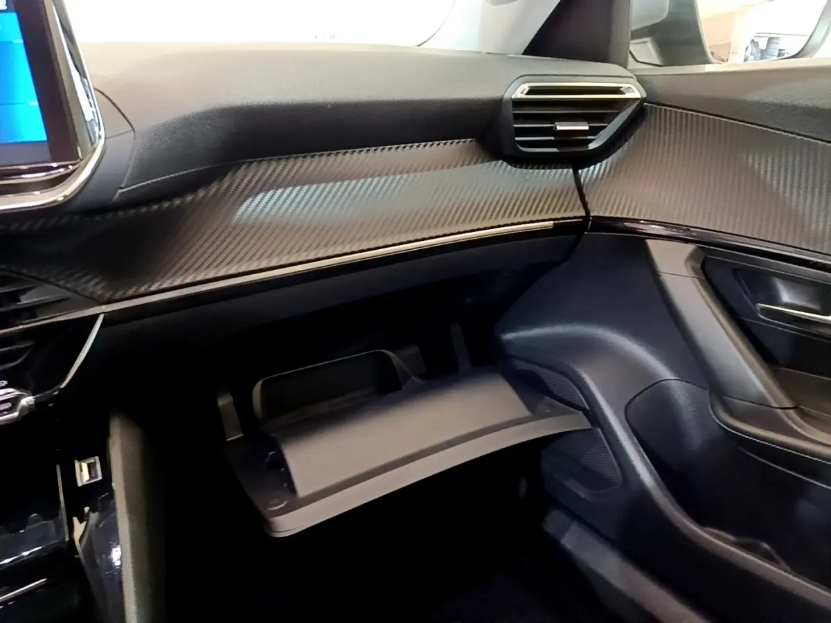 Intérieur côté passager du Peugeot 2008 gris clair 2021, tableau de bord avec finition carbone et boîte à gants ouverte.