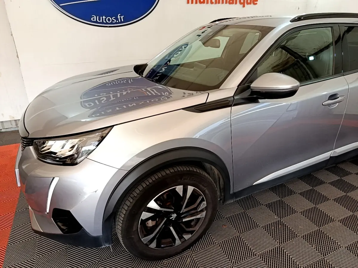 Vue 3/4 avant droit d’un Peugeot 2008 gris clair avec jantes noires et feux LED diurnes allumés.