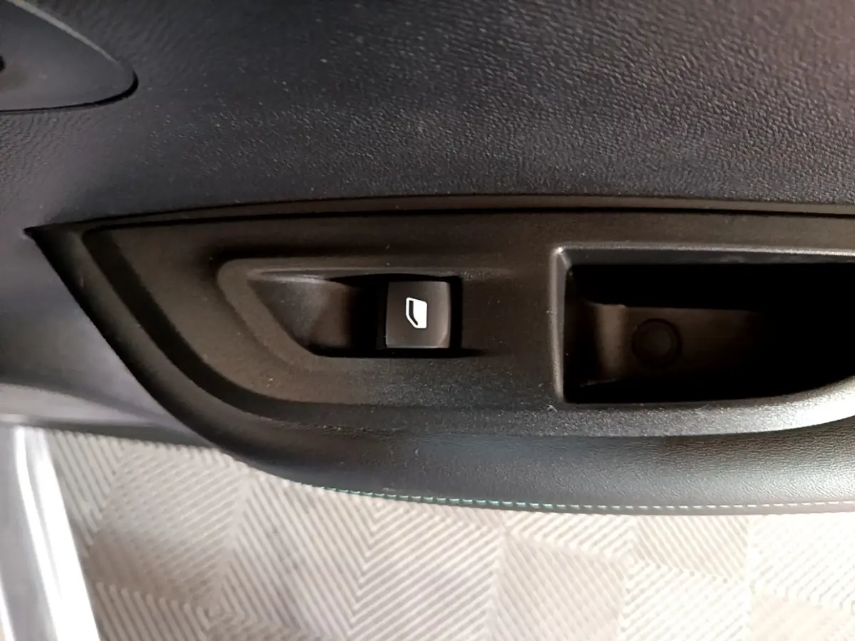Gros plan sur le bouton de commande de vitre électrique côté conducteur dans l'habitacle noir d'une Peugeot 2008 gris clair.